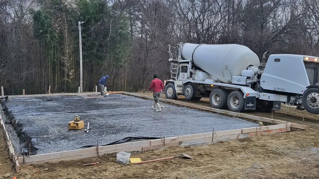 Concrete truck pouring concrete into a prepared foundation. Two workers in the construction site.