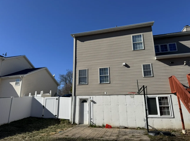 Backyard with white fence and beige townhouse under a clear blue sky