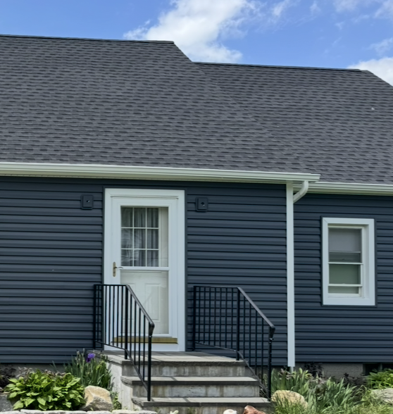 Blue house exterior with a white door, front steps, and black railings under a cloudy sky