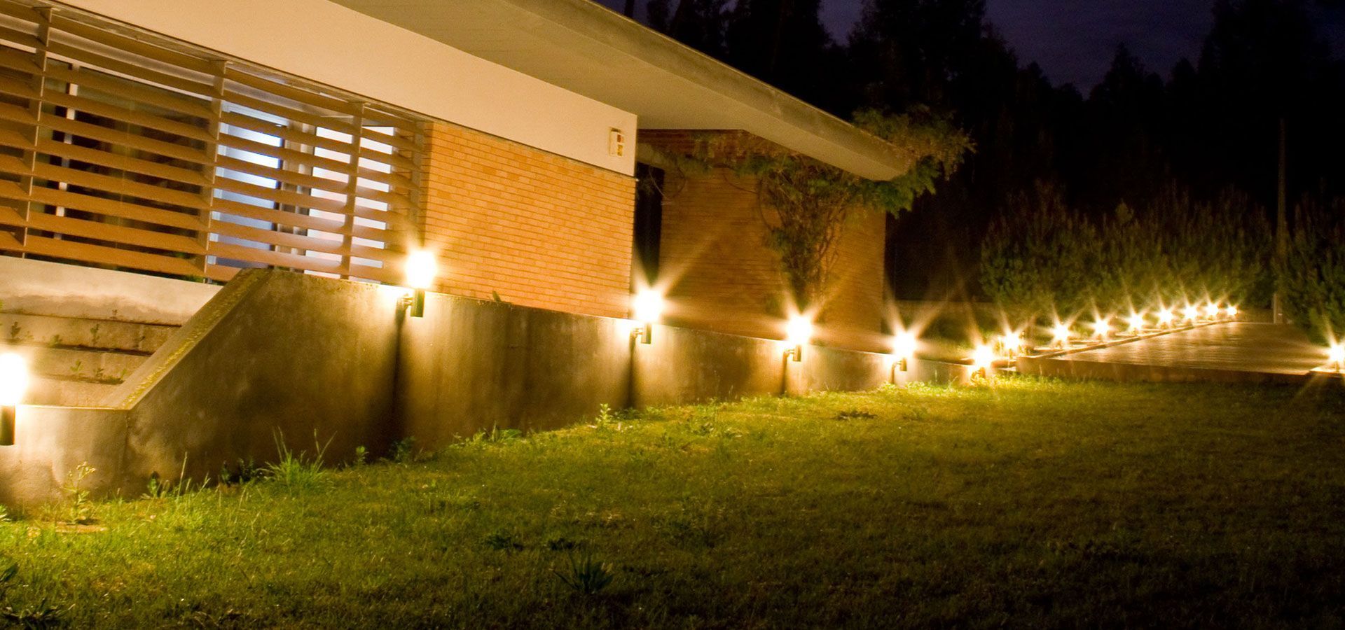 Man installing a wall-mounted light fixture on a house exterior in bright sunlight