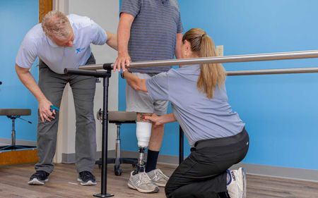 A woman is helping a man with a prosthetic leg walk.