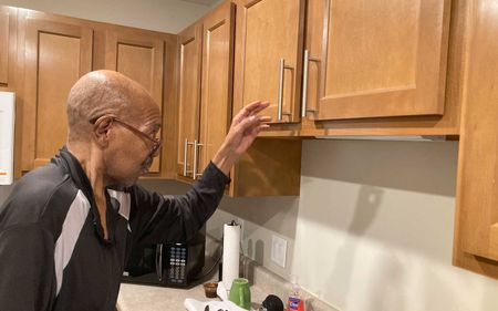 A man is standing in a kitchen reaching for a cabinet door.