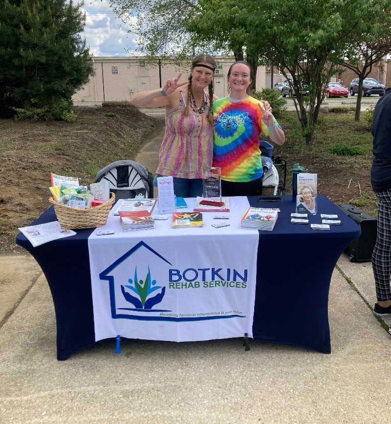 Two women are standing behind a table with a banner that says botkin rehab services.