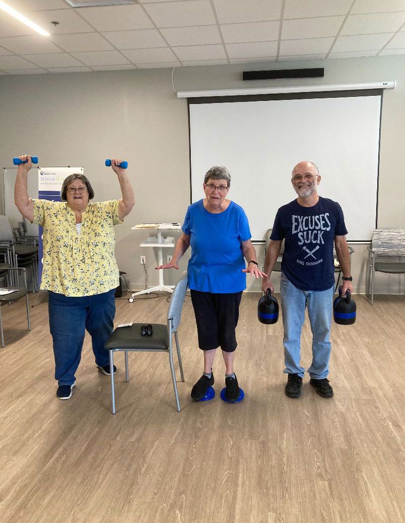 A group of people are standing in a room holding dumbbells.