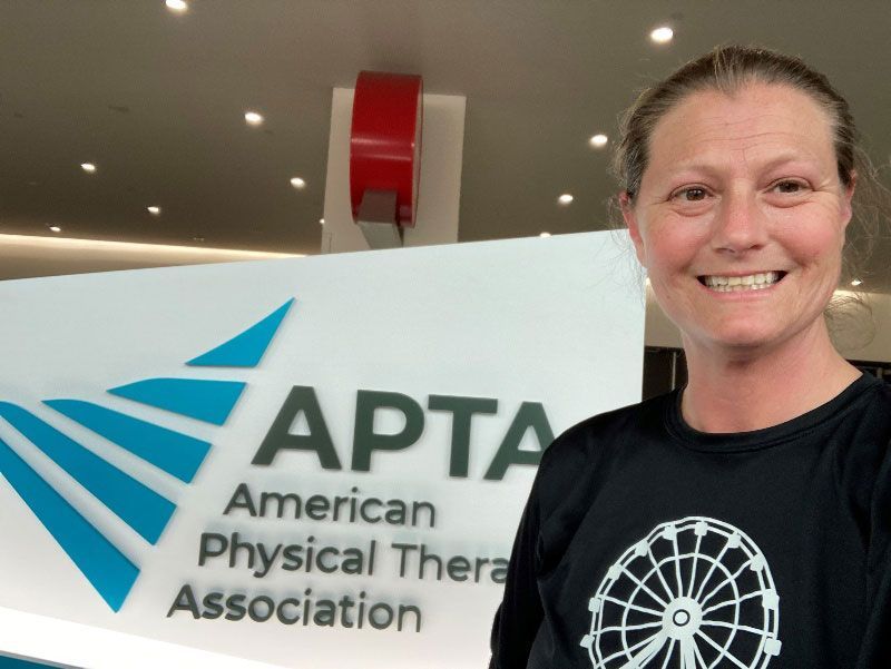 A woman stands in front of an american physical therapist association sign