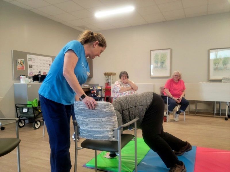 A woman in a blue shirt is helping a man in a chair