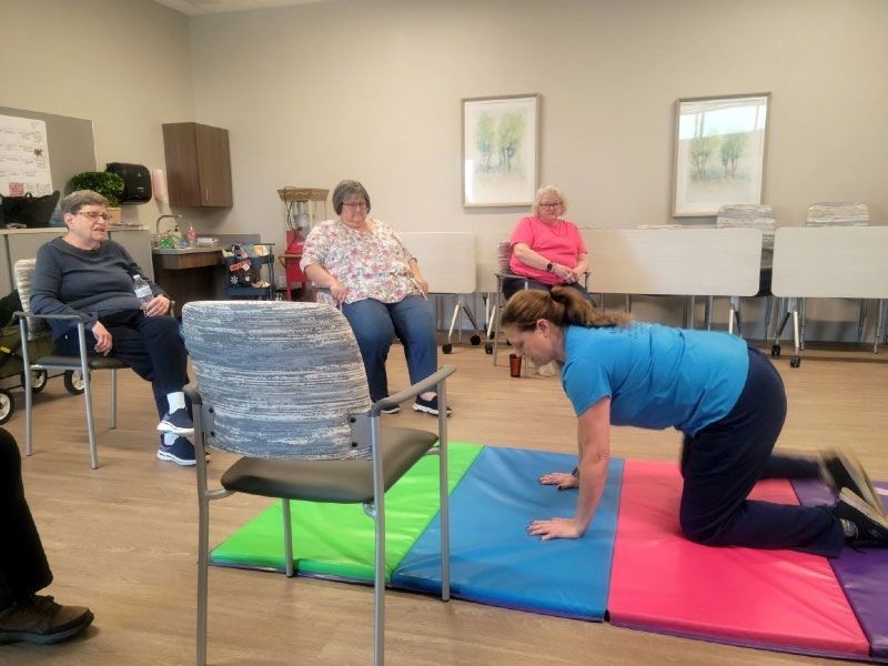 A woman is kneeling on a mat in a room with other people sitting in chairs.
