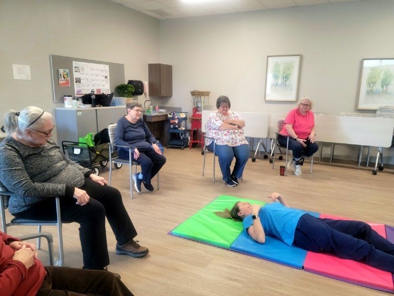 A group of women are sitting in chairs and laying on mats in a room.