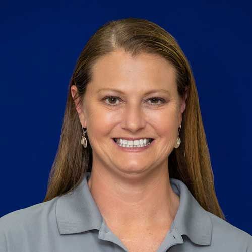 A woman wearing a gray shirt and earrings is smiling for the camera.