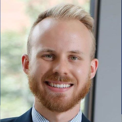 A man with a beard is smiling for the camera while wearing a suit and striped shirt.