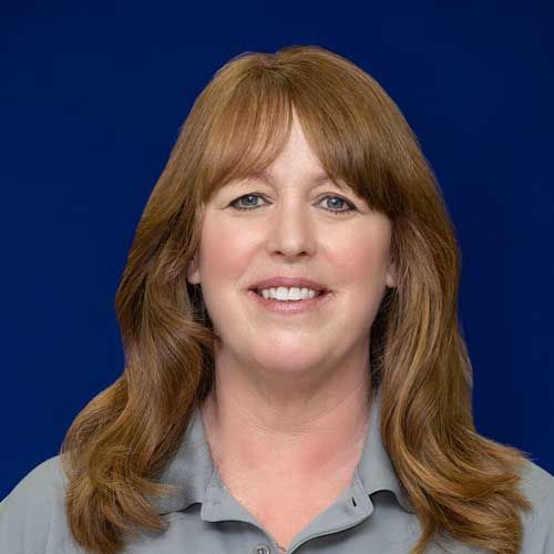 A woman with long brown hair is smiling for the camera in front of a blue background.