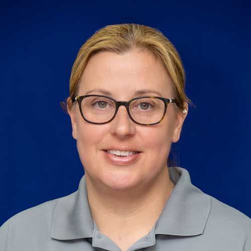 A woman wearing glasses and a grey shirt is smiling for the camera.