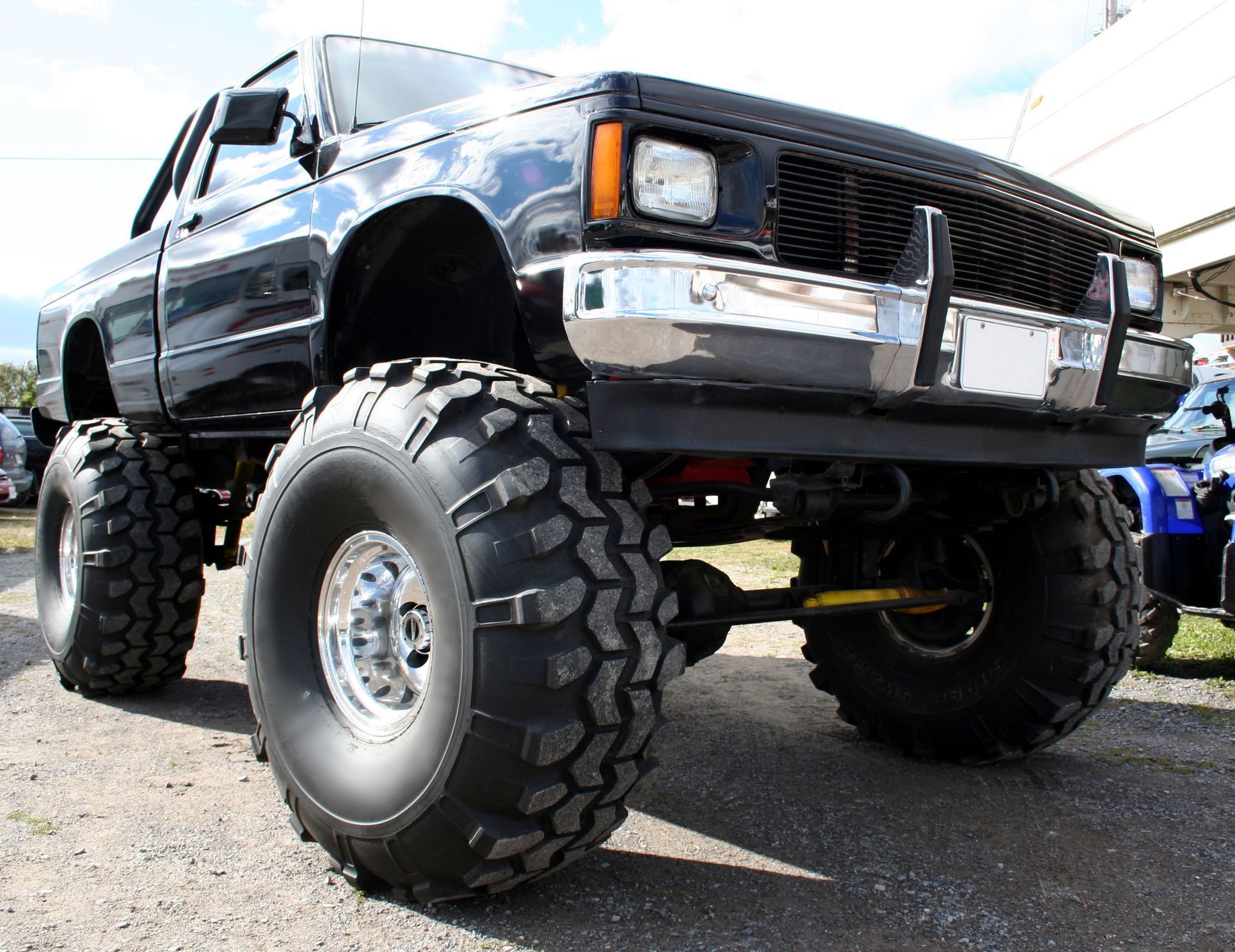 Black monster truck with huge tires, chrome bumper, and a black grille.