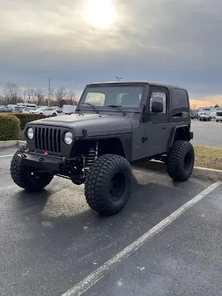 Black Jeep Wrangler with large off-road tires parked in a lot on an overcast day.