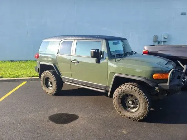 Green Toyota FJ Cruiser with black wheels and a black roof parked in a parking lot.