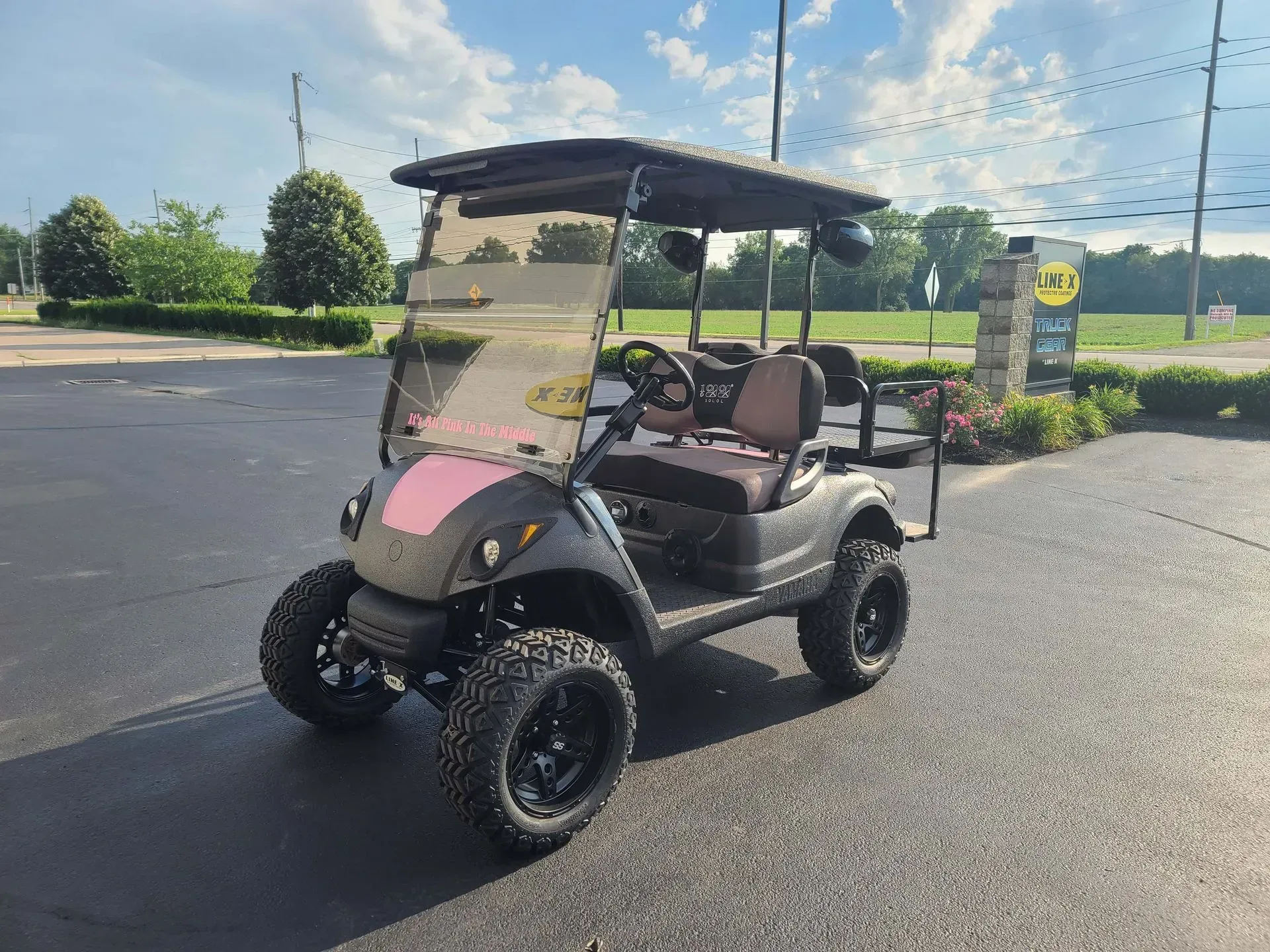 Black and pink golf cart with large tires, parked outside on pavement.