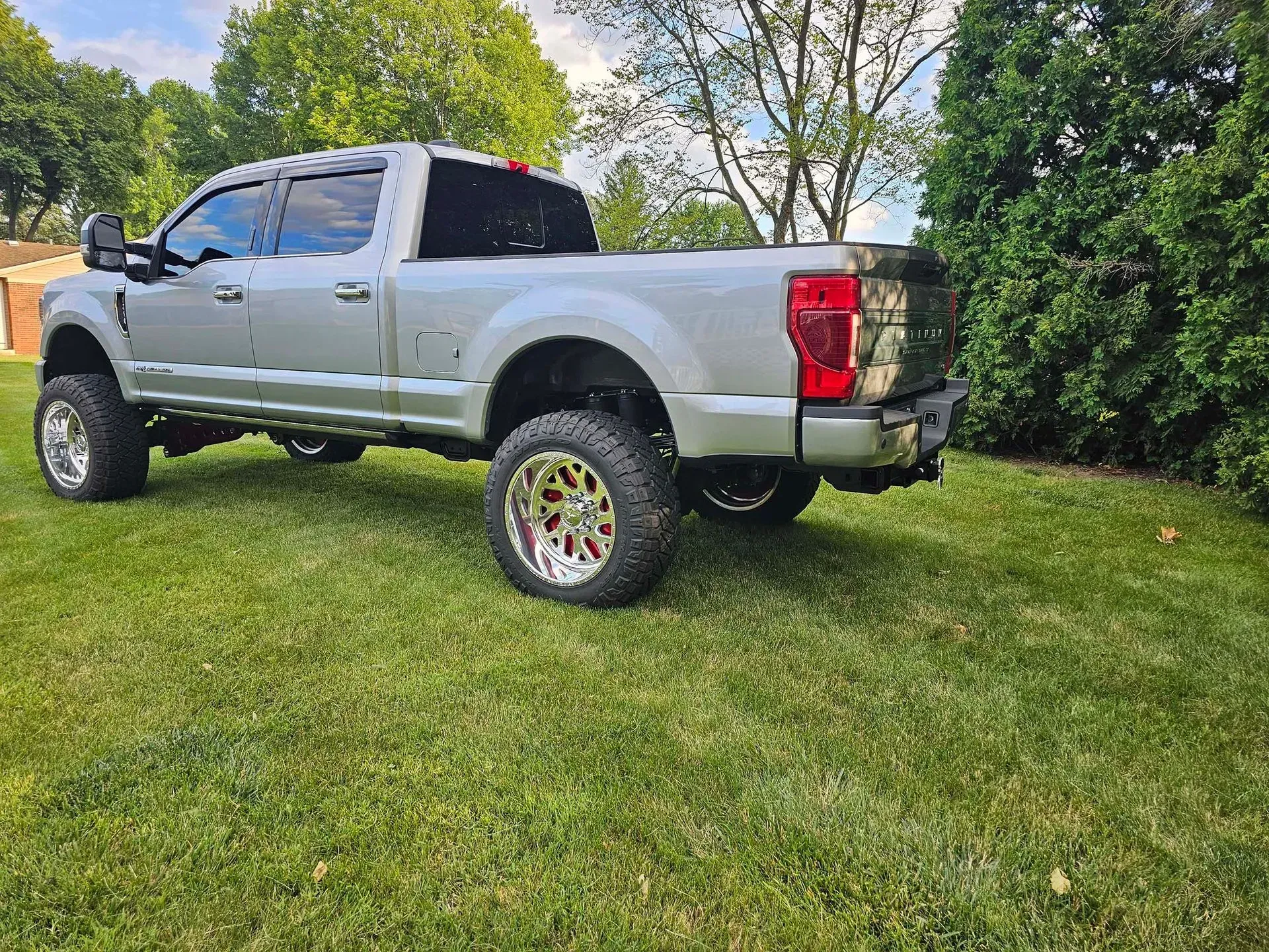 Silver pickup truck on grass lawn, bright chrome wheels, trees in background.