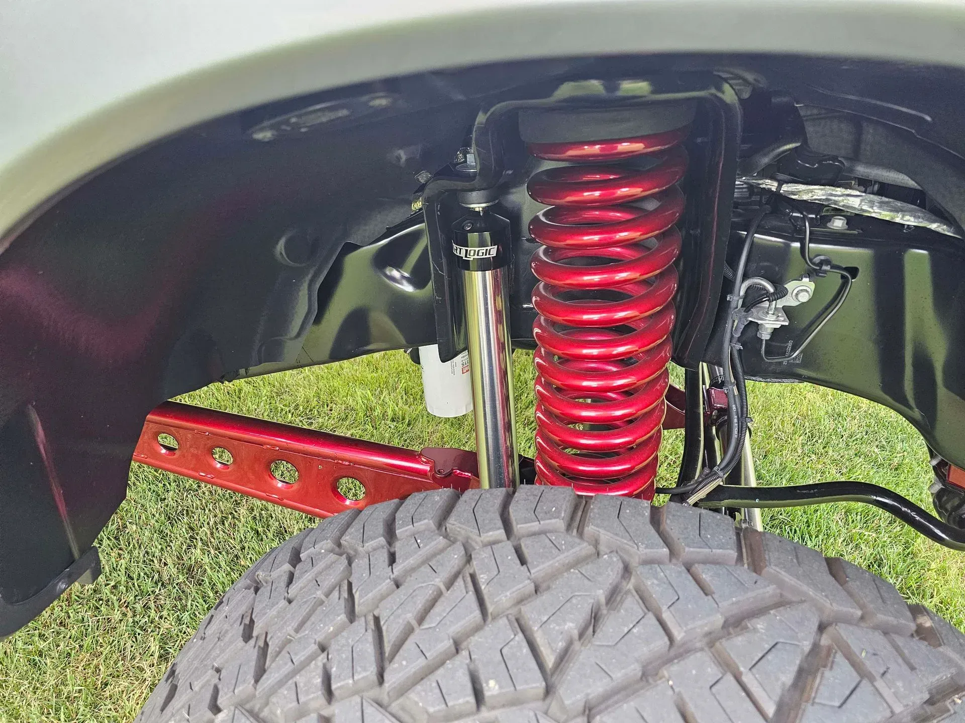 Red coil spring suspension and tire viewed inside a vehicle's wheel well.