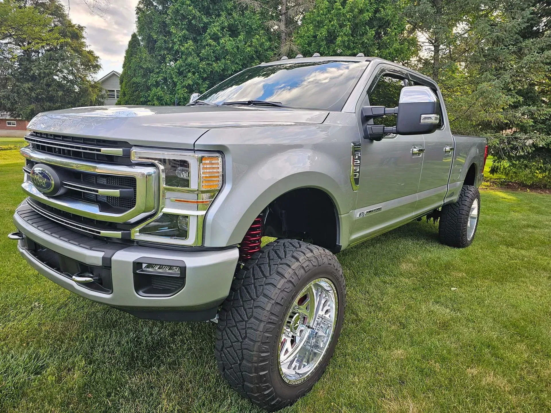 Silver Ford truck, lifted with large chrome wheels and tires, parked on grass.
