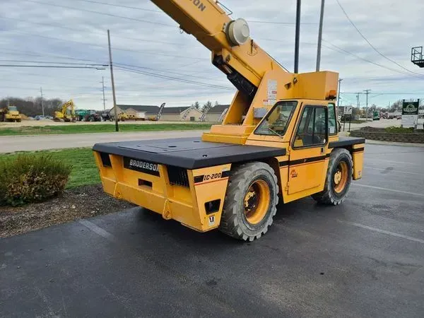 Yellow industrial crane on asphalt, parked outside, cloudy sky.