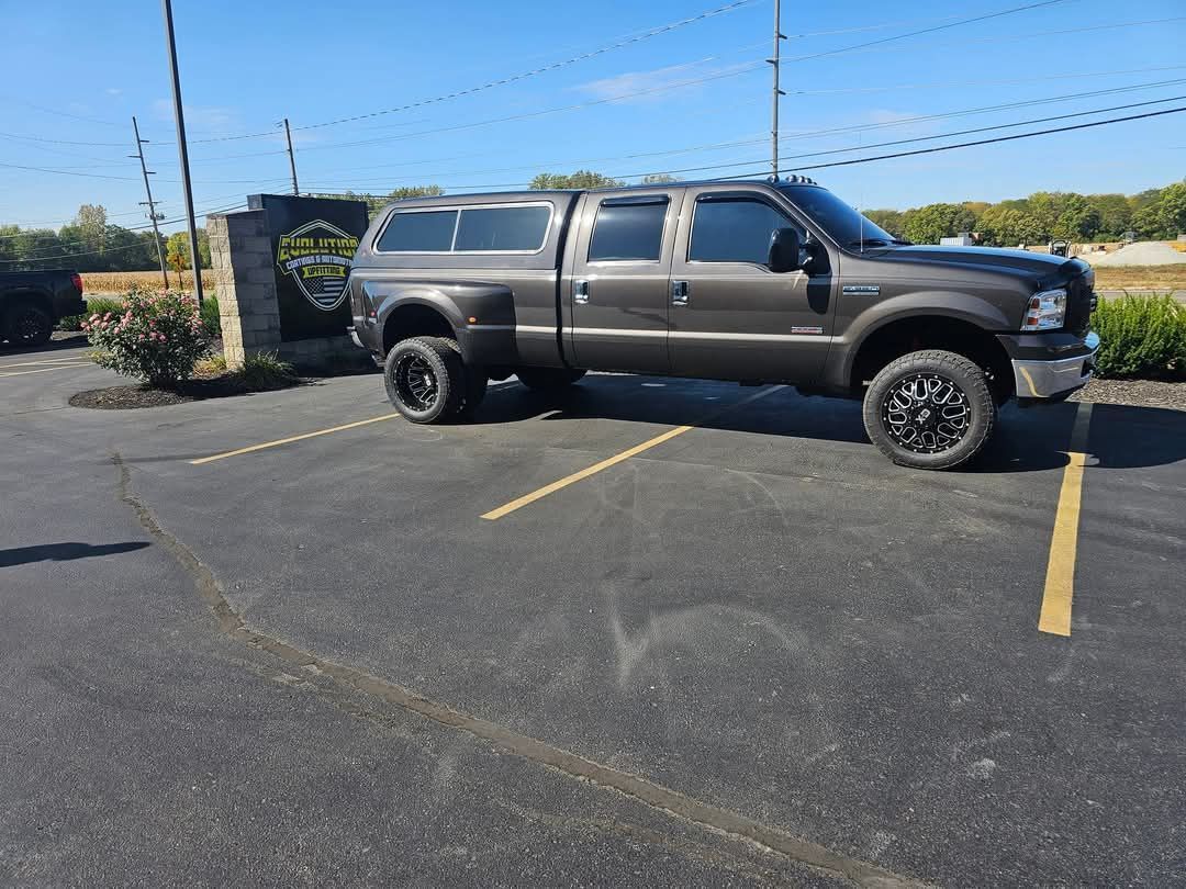 Dark gray Ford truck with a cap parked on asphalt in a parking lot.