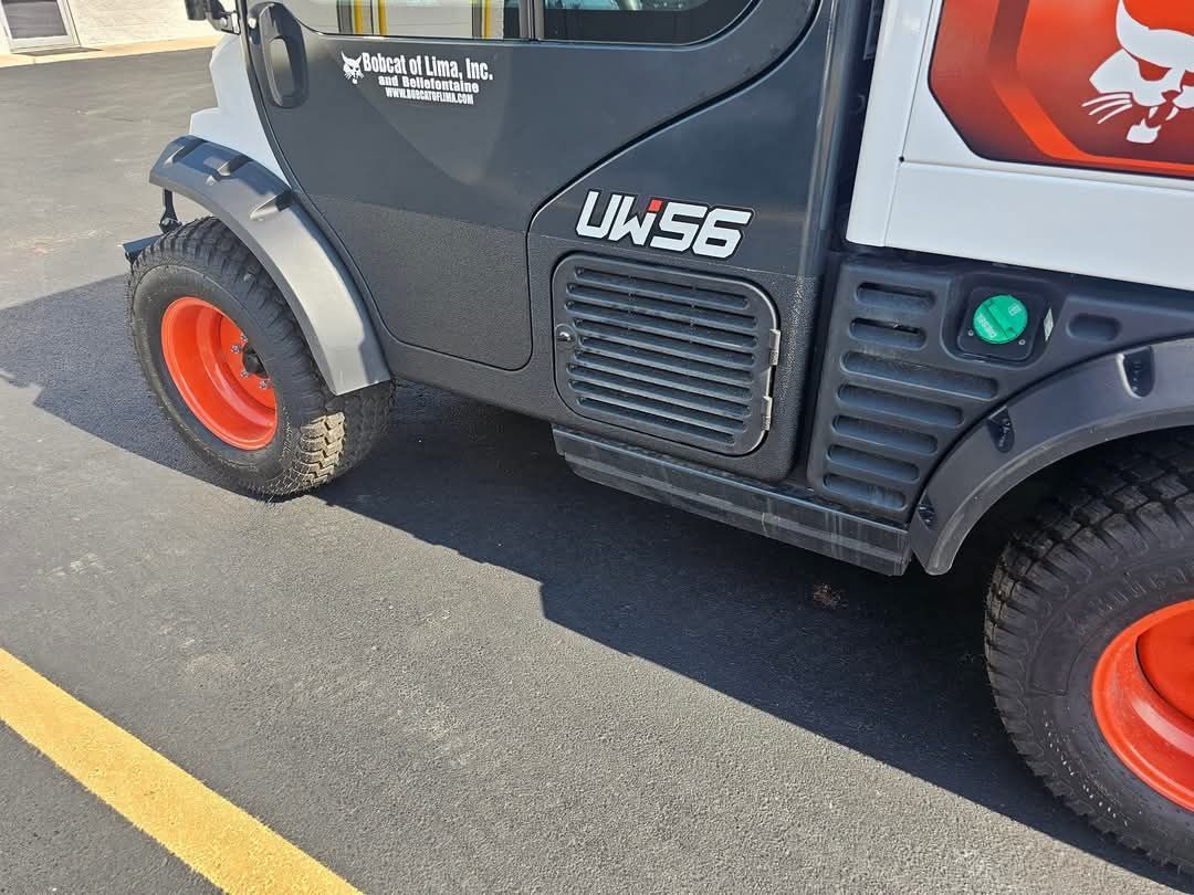 Black Bobcat UW56 utility vehicle with orange wheels on asphalt, next to a yellow line.