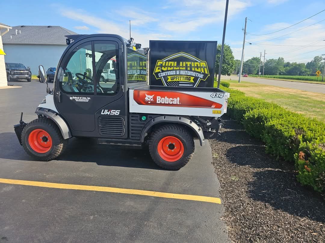 Bobcat utility vehicle parked next to a row of bushes; black and white with orange wheels.