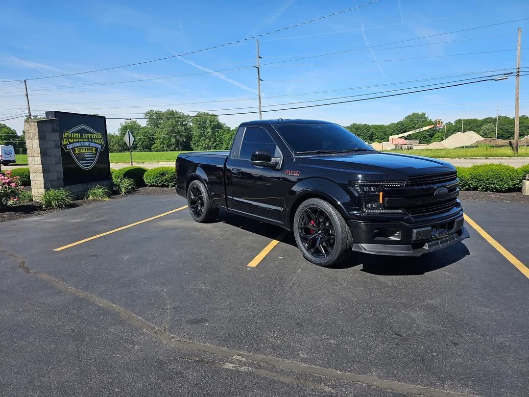 Black Ford F-150 pickup truck with tinted windows parked in a parking lot on a sunny day.