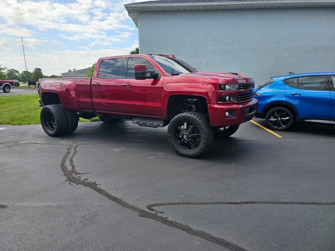 Red lifted pickup truck parked in an asphalt lot next to a blue car.