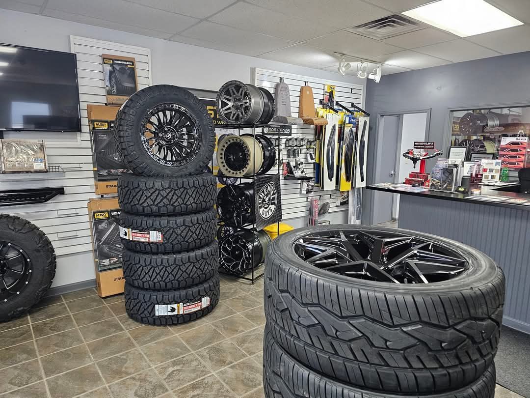 Tires stacked in a tire shop. Black and silver rims are visible in a bright, clean interior.