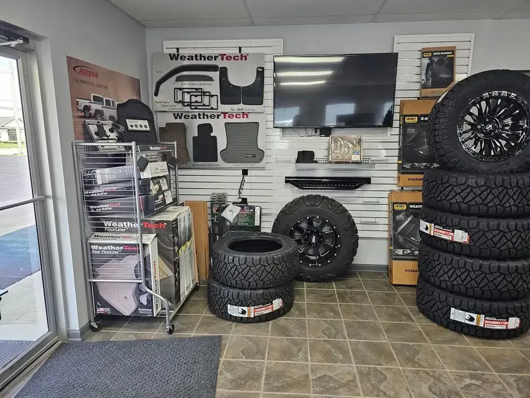 Interior of a tire shop. Tires stacked, WeatherTech mats on display, TV, and shelving with auto accessories.