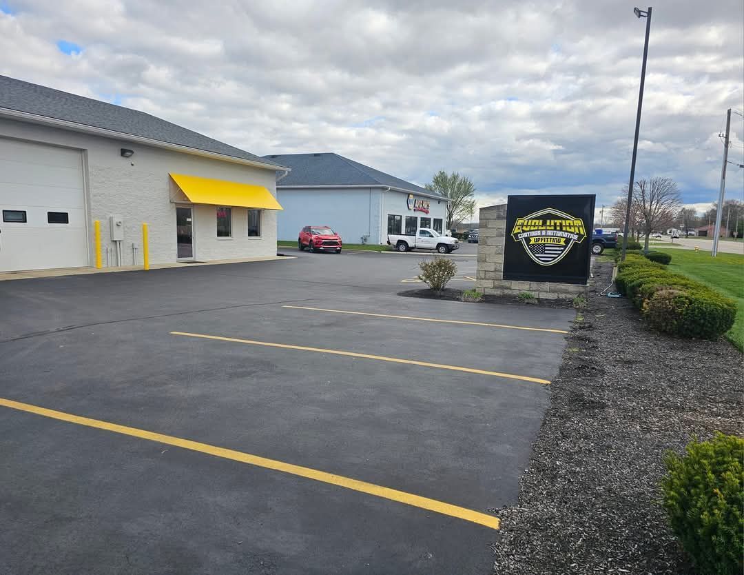 A paved parking lot with a yellow awning building and a business sign on a cloudy day.