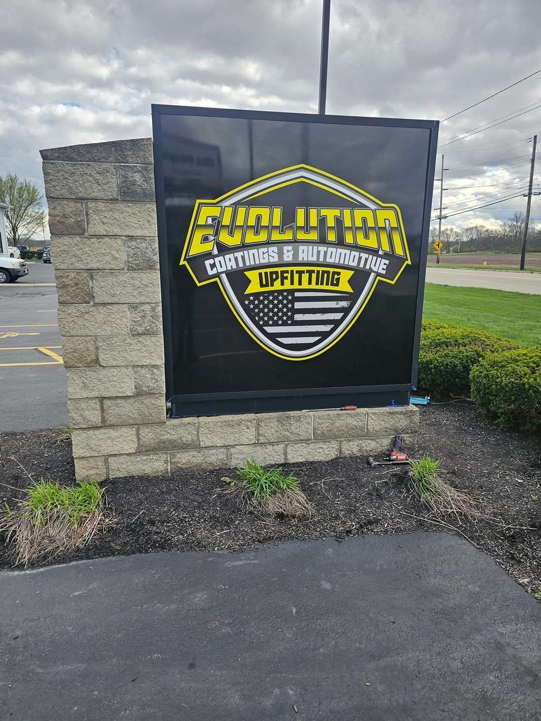 Sign for Evolution Customs & Auto Repair, black with yellow text and American flag.