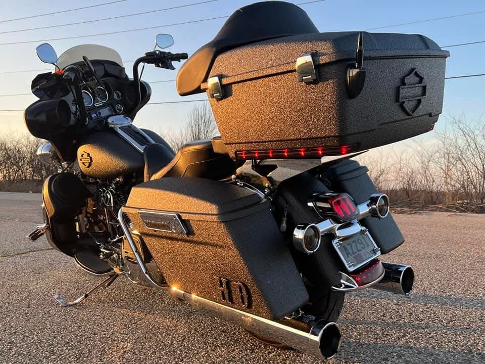 Black Harley-Davidson motorcycle with textured finish, large trunk and saddlebags, chrome exhaust, parked outdoors at sunset.