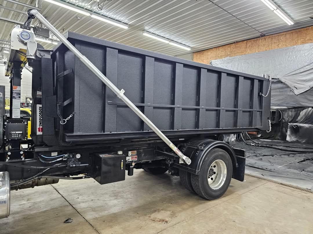 Black dump truck in a garage, with a silver support beam.