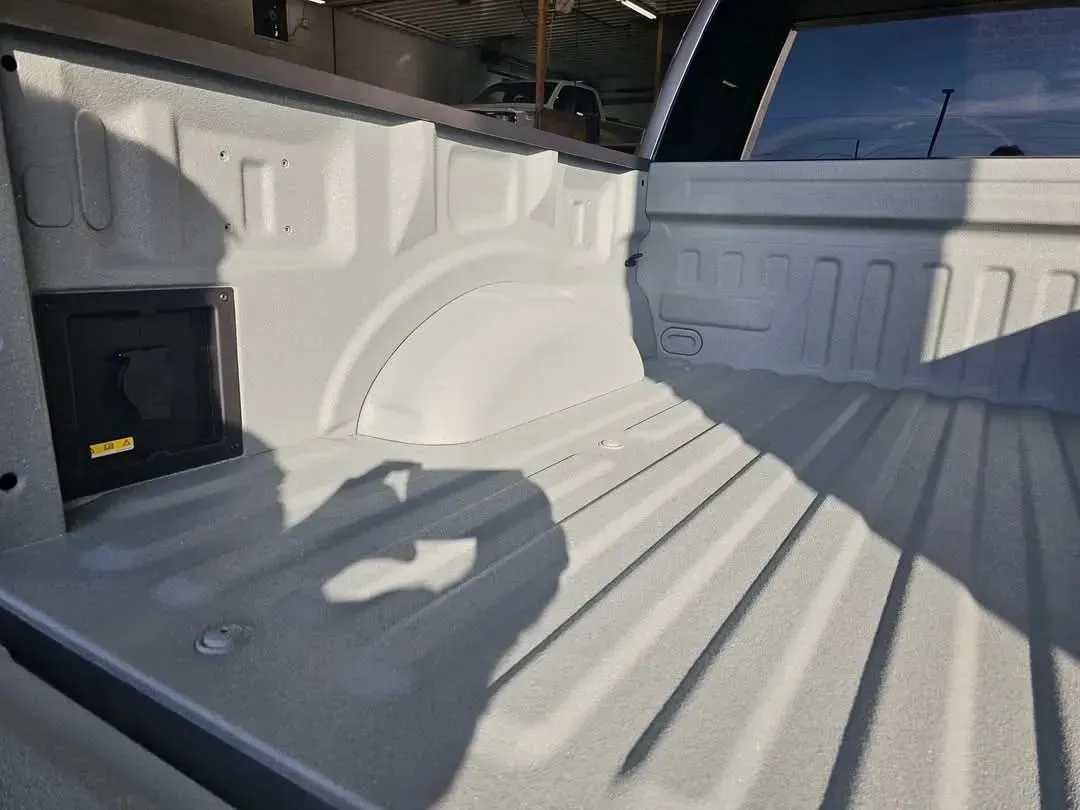 Inside of a truck bed coated in light grey spray-on bedliner. A subwoofer is mounted on the left.