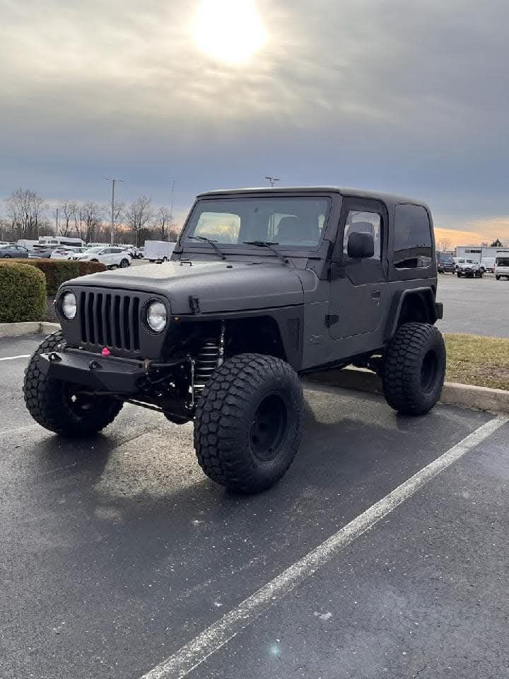Black lifted Jeep Wrangler parked on asphalt under a cloudy sky.