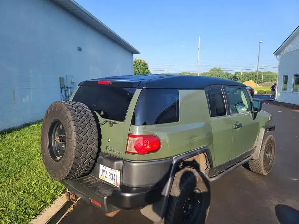 Green Toyota FJ Cruiser SUV with spare tire, parked beside a building.