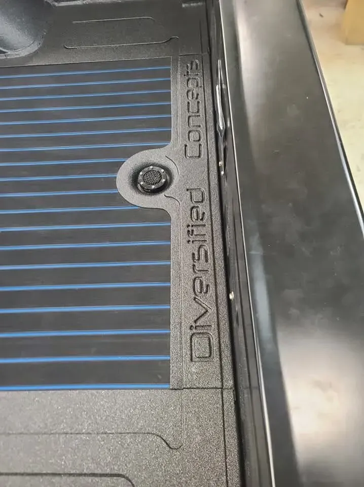 Close-up of a truck bed with a textured liner by Diversified Concepts, showing a black anchor point and a blue stripe.