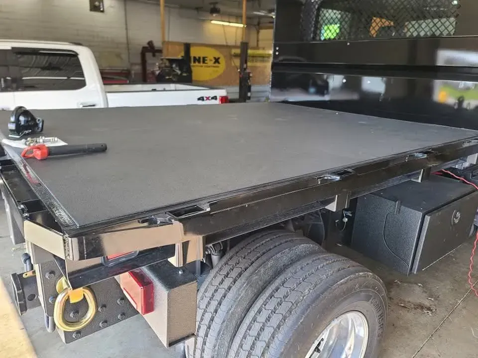 A black flatbed truck with a covered bed, likely in a garage.  The bed has a smooth, dark surface.