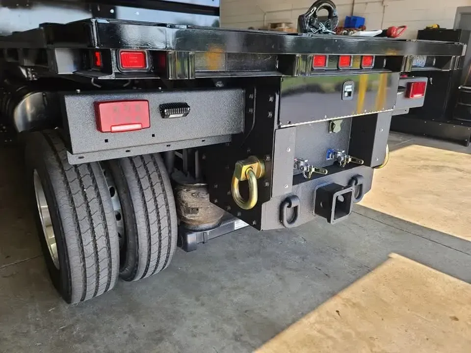 Rear view of a black flatbed truck with dual rear wheels, showing hitch, lights, and tow ring.
