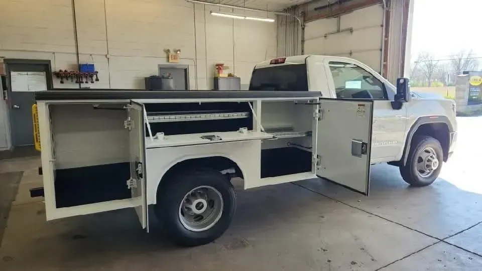 White work truck with open tool boxes inside a garage.