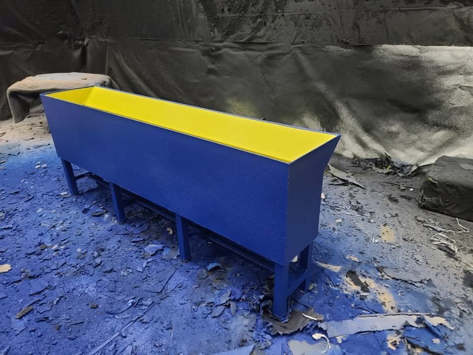 Blue and yellow rectangular planter box on short legs in a paint-splattered environment.