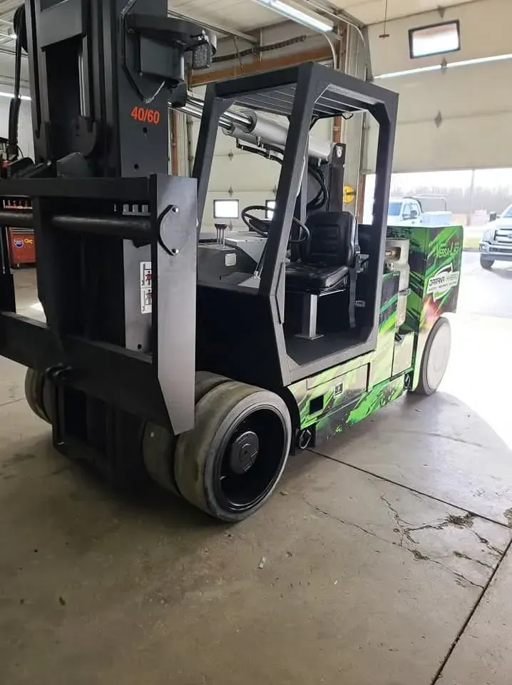 Black and green forklift in a garage with visible wheels and a driving cabin.