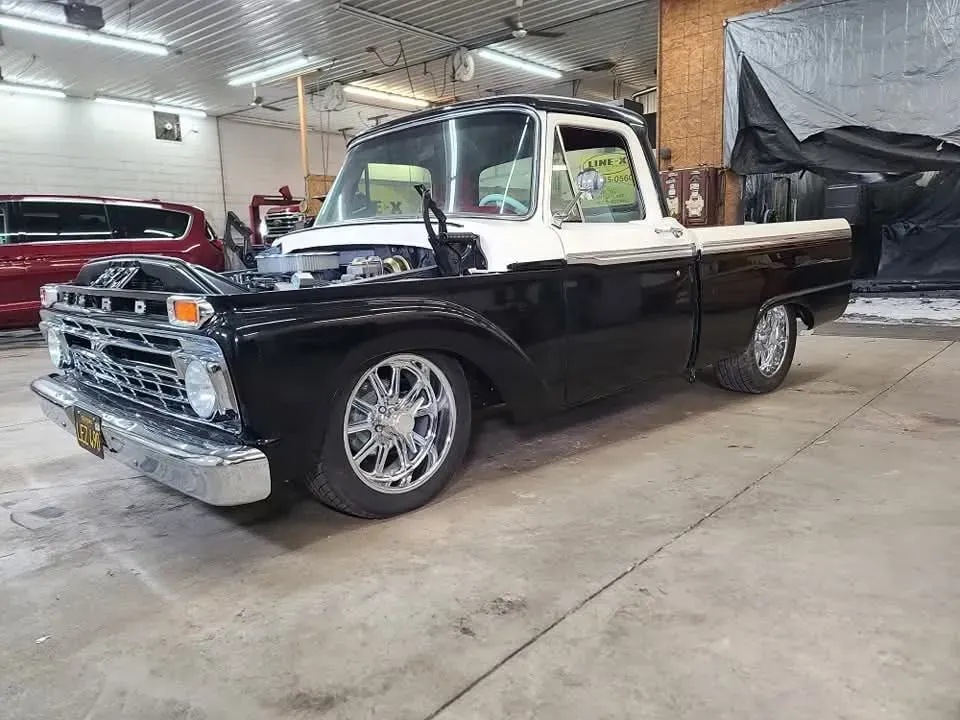 Black and white classic Ford pickup truck in a garage. Chrome wheels, lowered stance, engine visible.