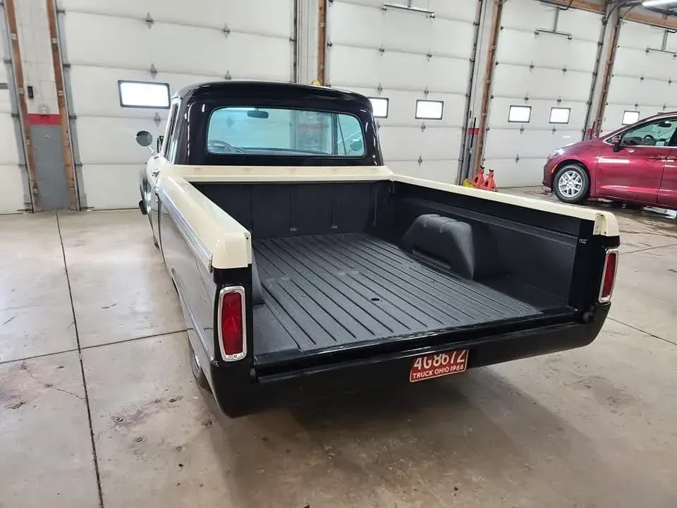 Black and cream vintage pickup truck with an empty bed in a garage.