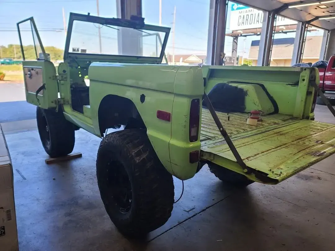 Lime green vintage Bronco with black wheels, doors open, tailgate down, in a shop.