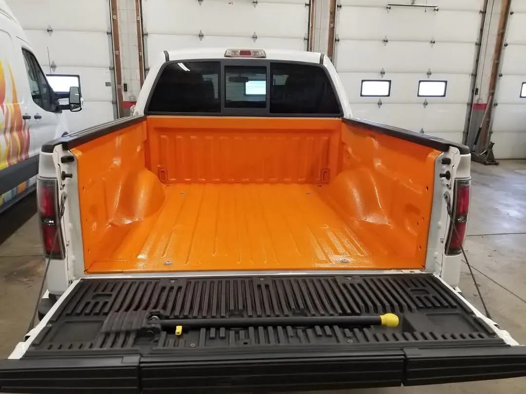 White pickup truck bed interior, painted orange, tailgate down with equipment.