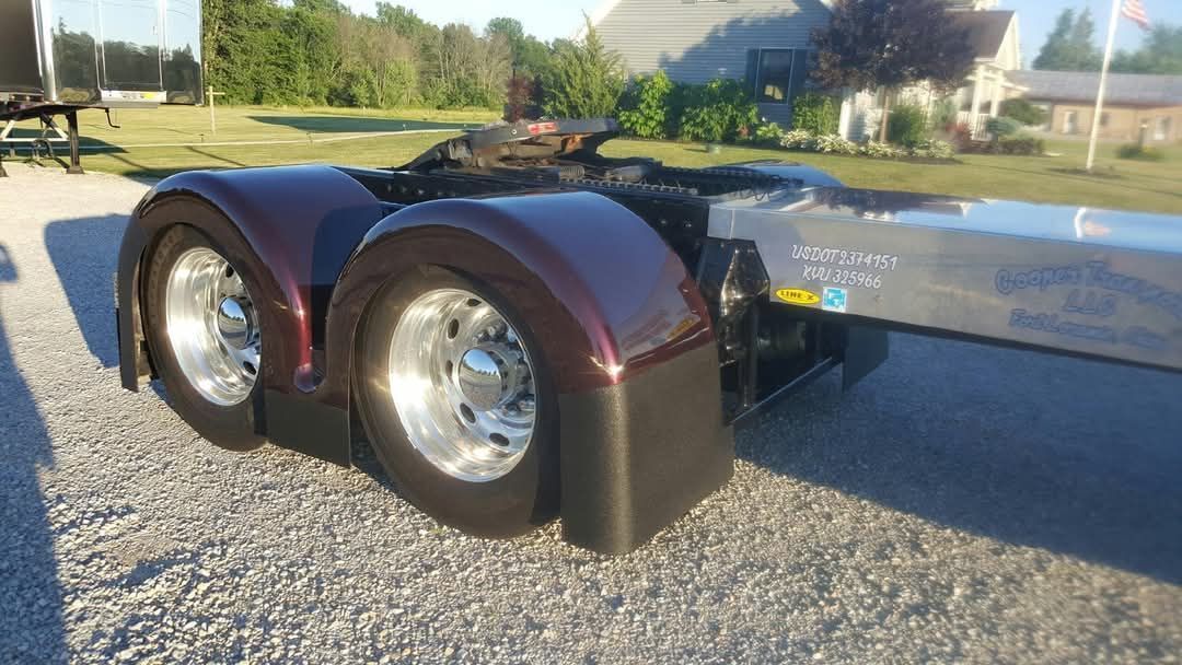 Burgundy truck fenders and polished wheels on gravel.