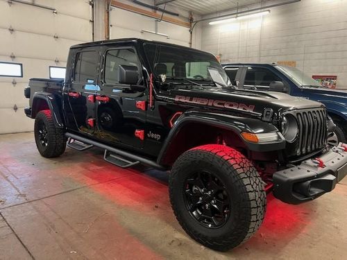 Black Jeep Gladiator Rubicon with red underglow in a garage.